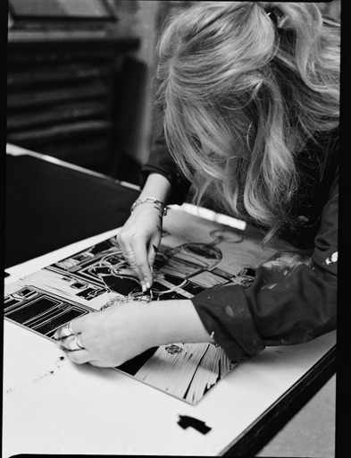 A woman is seen carving a design into a block of lino 