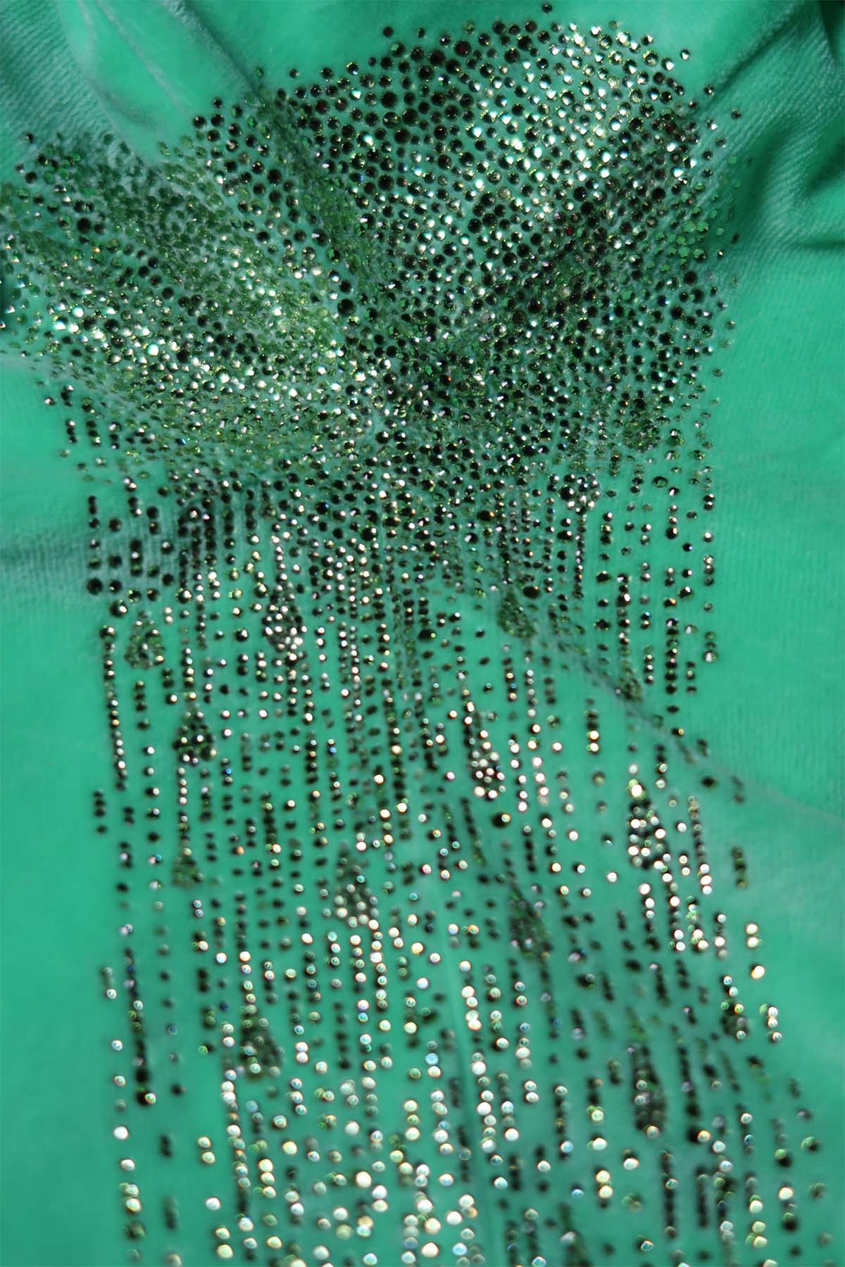 The unworn underarm area of a bright green velour tracksuit top. Small light green rhinestones are saturated at the armpit area like a sweat patch, and trail down in droplet shapes along the side-seam of the top.