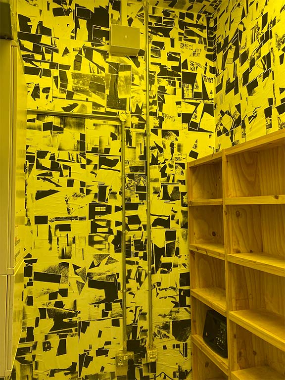 A room lit in yellow light wallpapered with black and white photocopy collages