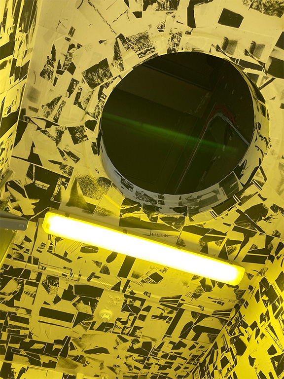 a room lit in yellow light with black and white photocopied collages wallpapered on