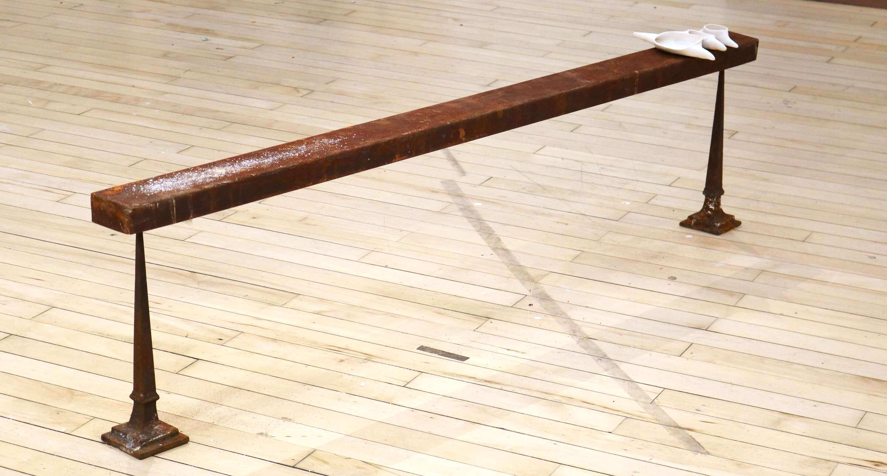 A rusted steel narrow bench on narrow legs, 2 metres long, 60 centimetres high and 10 centimetres wide. At one end are placed 3 white ceramic vessels in ascending size containing traces of salt. At the other end of bench there is a sprinkled line of salt.