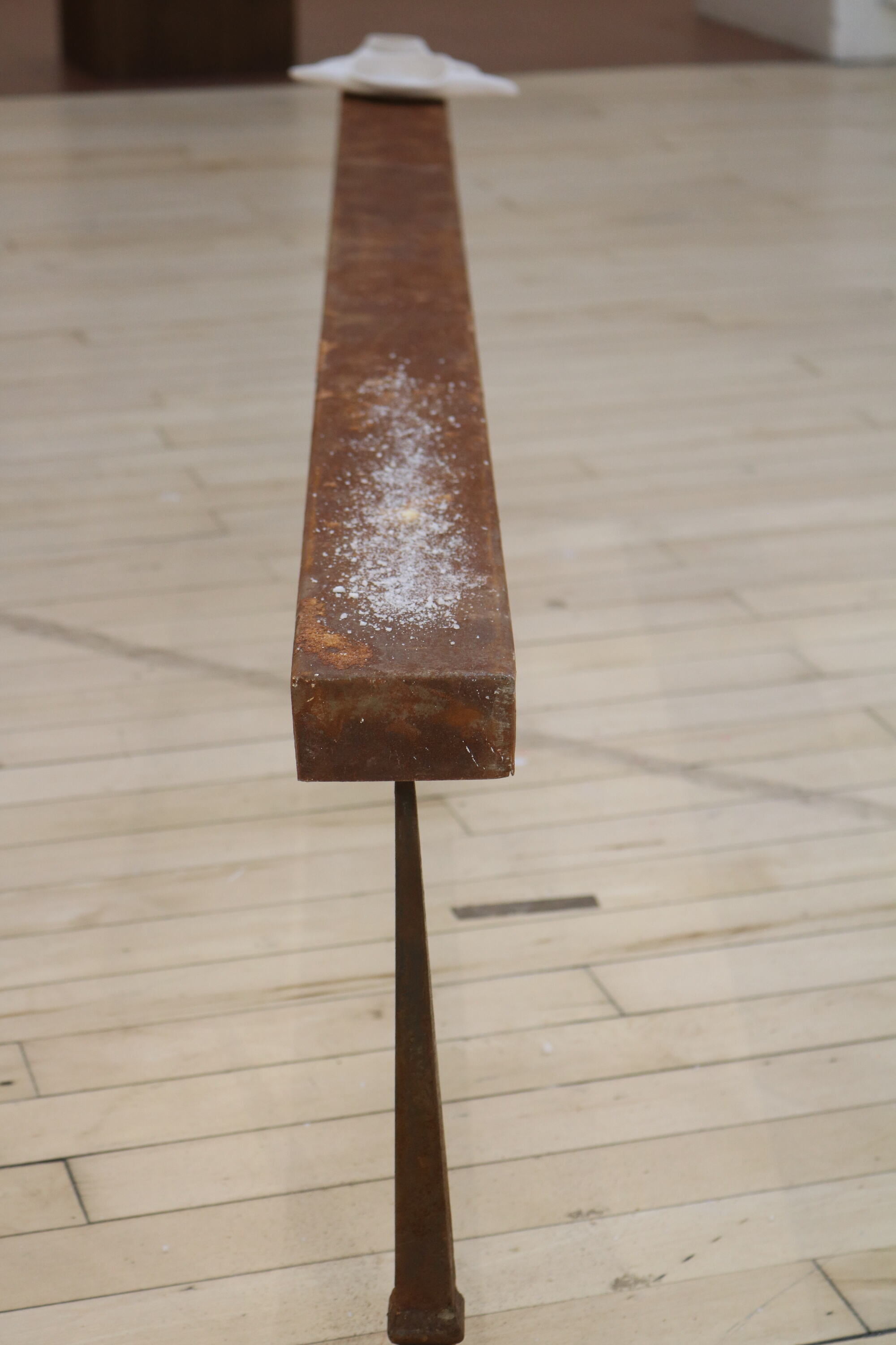 A rusted steel narrow bench on narrow legs, 2 metres long, 60 centimetres high and 10 centimetres wide. At one end are placed 3 white ceramic vessels in ascending size containing traces of salt. At the other end of bench there is a sprinkled line of salt.