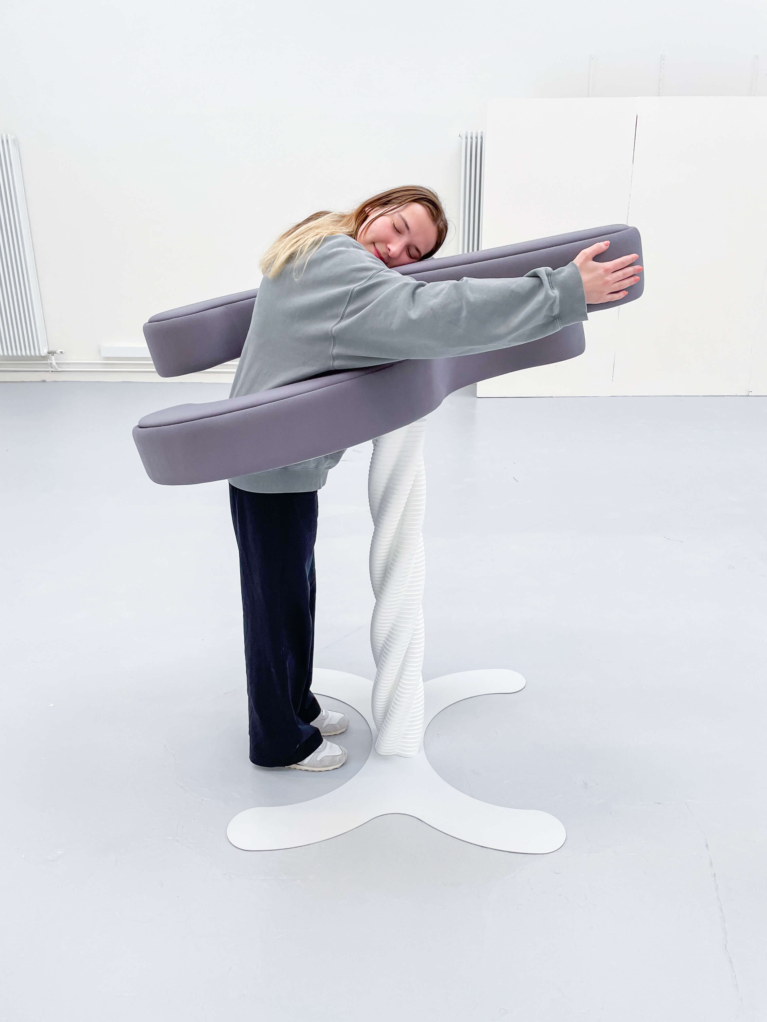 Positioned as a free-standing hugging reciprocal, Embrace assumes a prominent presence within the user's domestic environment while simultaneously stimulating discourse and reflection. Its visually striking design, characterized by elegant and simplistic curves, embodies the inherent simplicity and accessibility of the product.