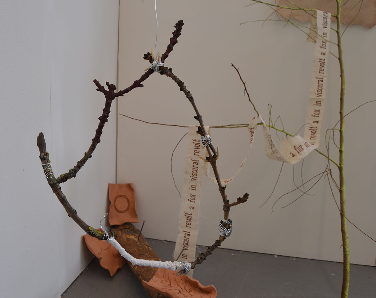 Wooden hoop hanging in front of clay tiles with letterpress words and spray painted branch in the background