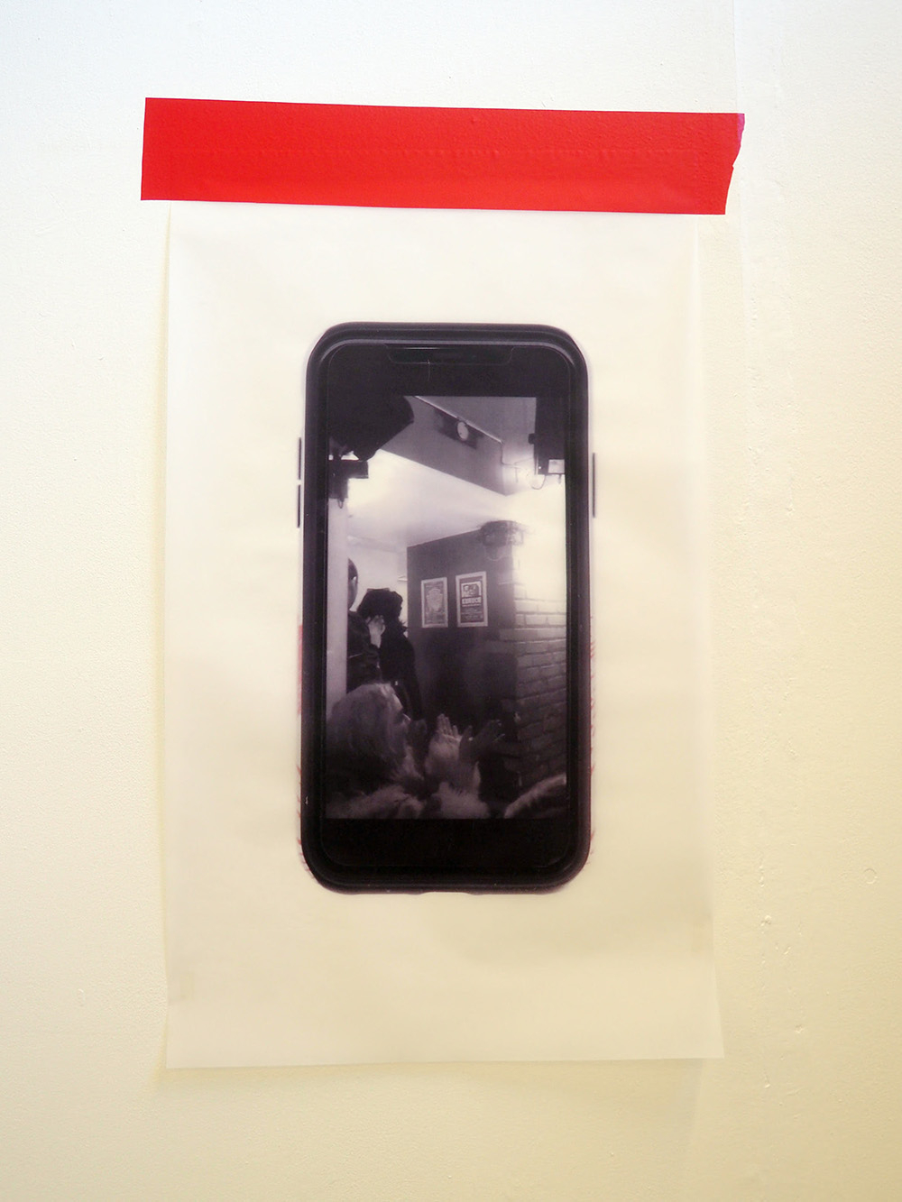 Print of a phone screen onto acetate, taped to the wall with red vinyl.