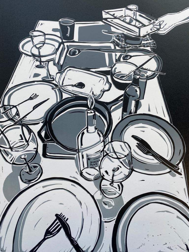 Dishes and plates sit on a table after a meal. A hand extends to pick up a plate
