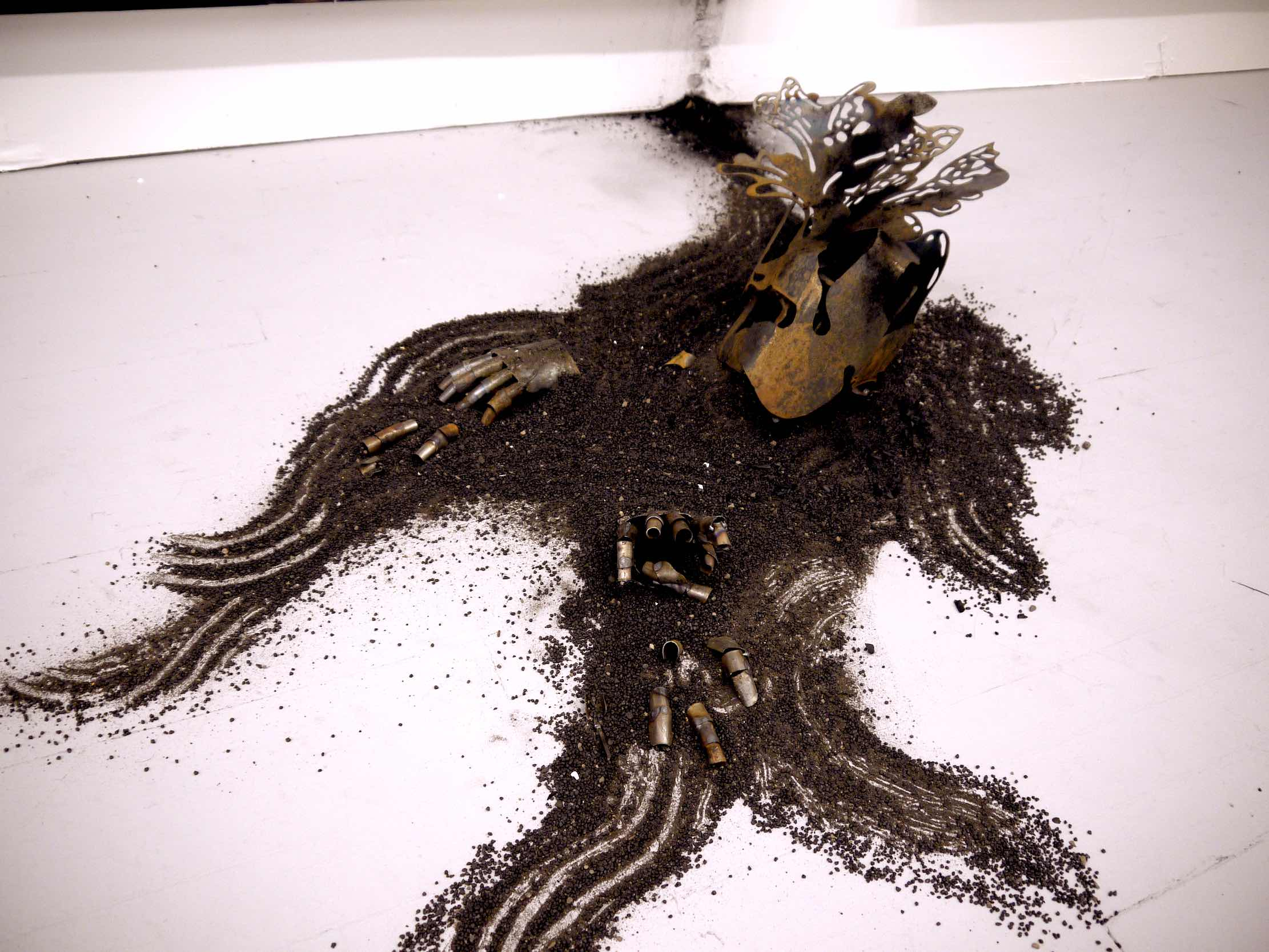 figurative steel sculpture situated on the floor, embedded in arranged gravel.