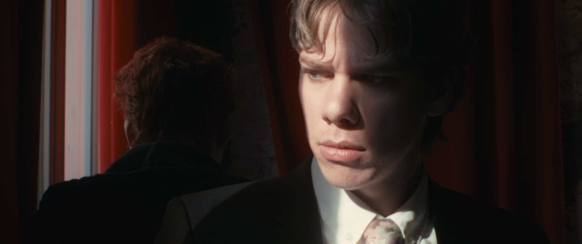 Young man sitting in the dark next to a window, the sun shines on his face