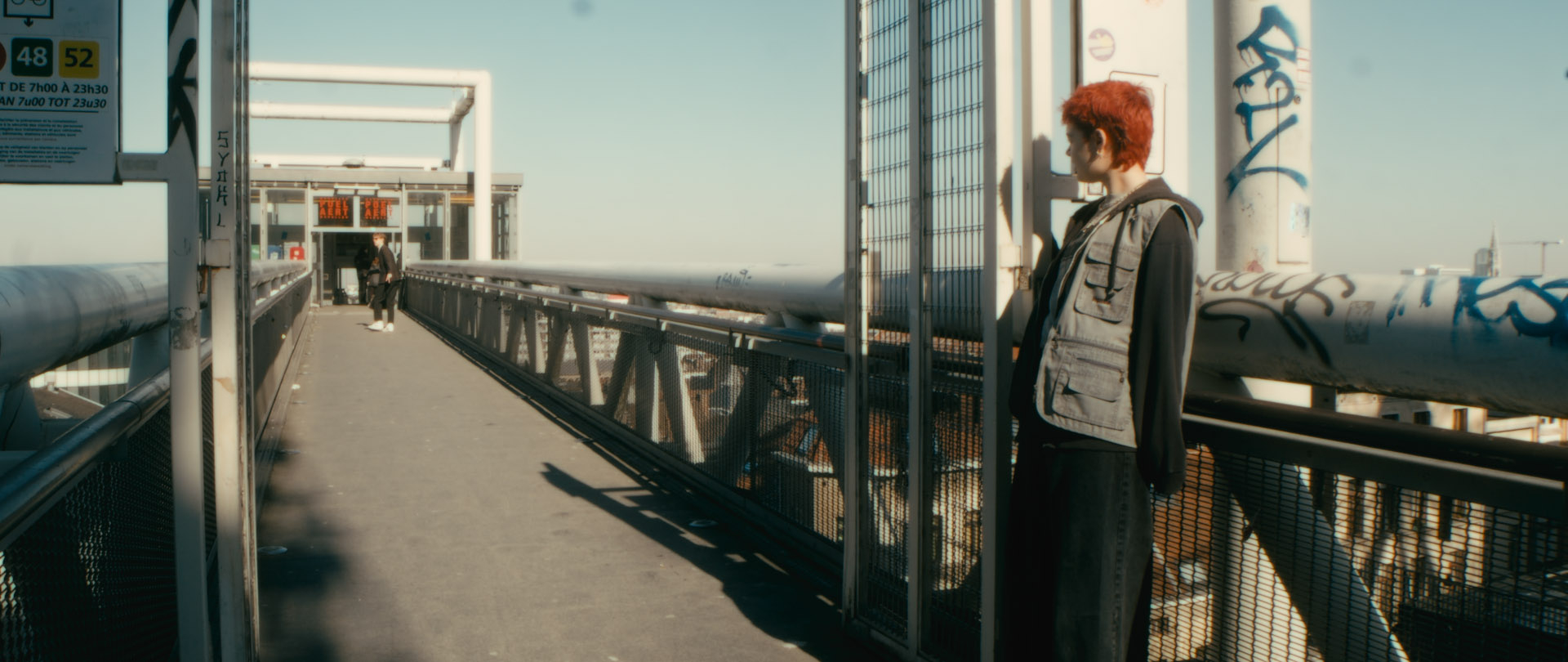 A person with short red head watches on a bridge how a man in a suit leaves