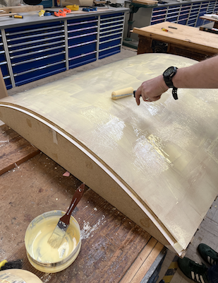A hand is adding glue to a large wooden surface with a roller