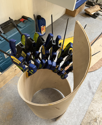 Top view of a wooden spiral, with blue clamps along one edge holding it together 