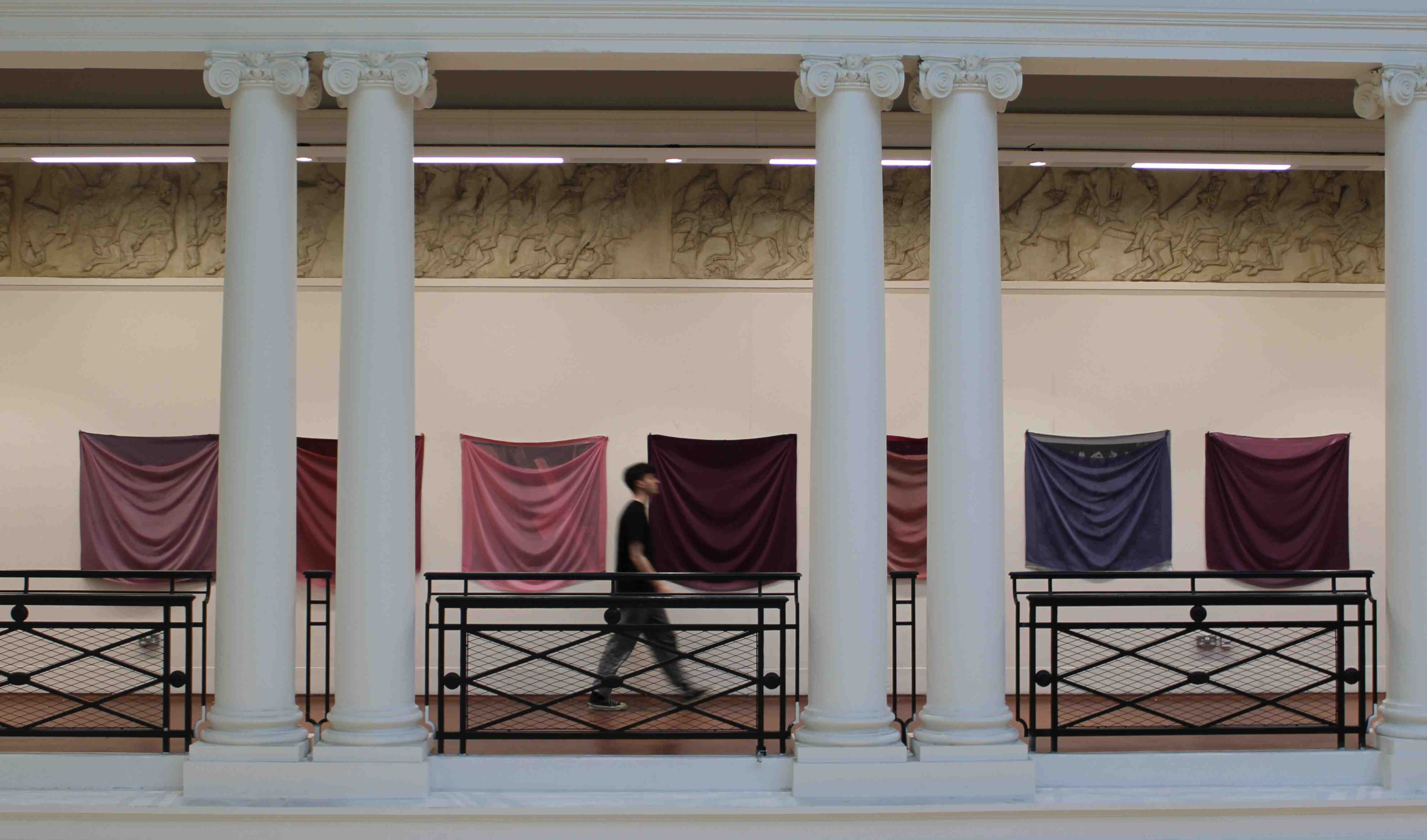 7 fabric squares on a wall with pillars in front of them and a person walking in front